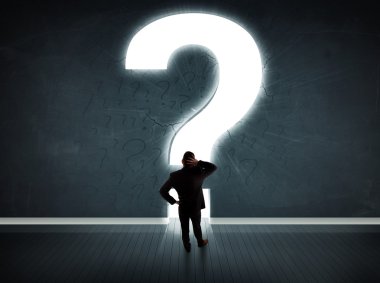 Parlak bir soru işaretiyle duvara bakan bir iş adamı 