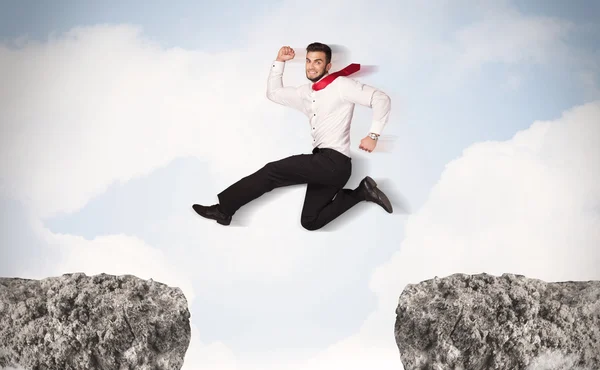 Забавный бизнесмен, прыгающий через скалы с разрывом — стоковое фото