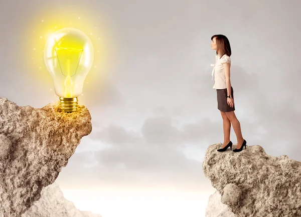 Businesswoman on rock mountain with idea bulb — Stock Photo, Image