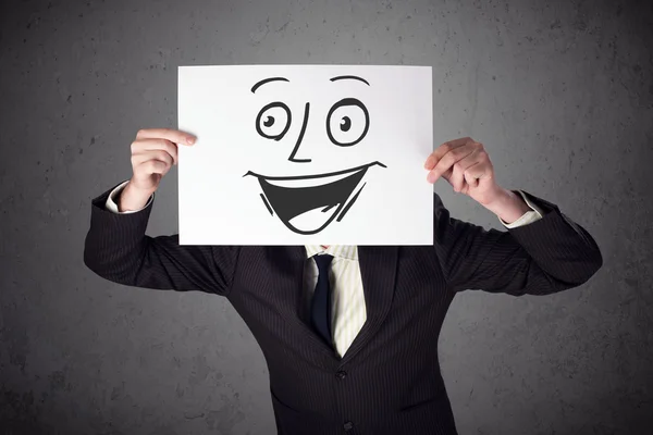 Businessman holding a cardboard with smiley face on it in front — Stock Photo, Image