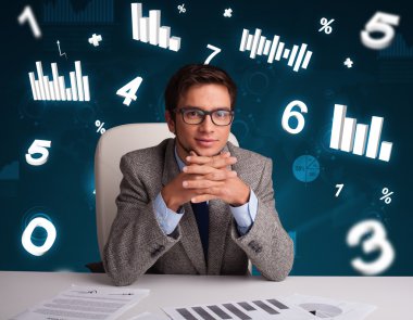 İş adamı masasında şema ve istatistiklerle oturuyor