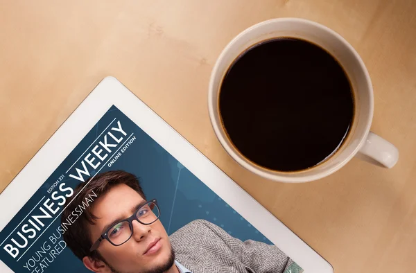 Tablet pc showing magazine on screen with a cup of coffee on a d