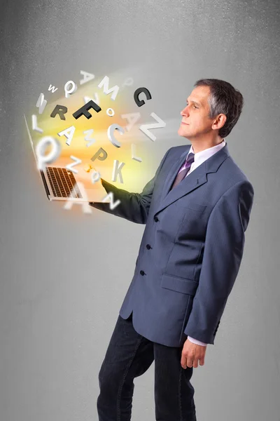 Middle aged businessman holding laptop with colorful letters — Stock Photo, Image