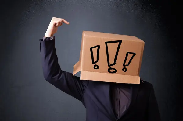 Young man gesturing with a cardboard box on his head with exclam — Stock Photo, Image