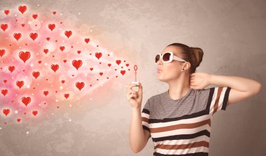 Güzel genç kız kırmızı kalp sembolleri üflüyor. 