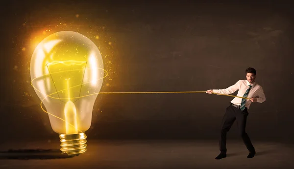 Business man pulling a big bright glowing light bulb — Stock Photo, Image