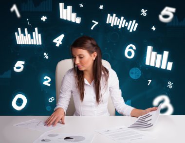 Masasında şema ve istatistiklerle oturan genç iş kadını.