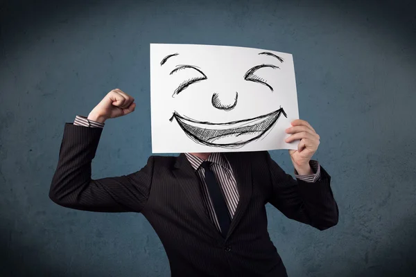 Бізнесмен тримає папір з усміхненим обличчям перед своїм обличчям — стокове фото