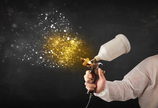 Worker with airbrush painting with glowing golden paint — Stock Photo, Image