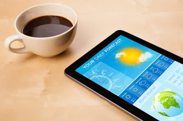 Tablet pc showing weather forecast on screen with a cup of coffe — Stock Photo, Image