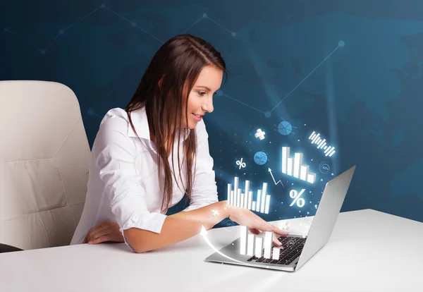 Pretty woman sitting at desk and typing on laptop with diagrams — Stock Photo, Image
