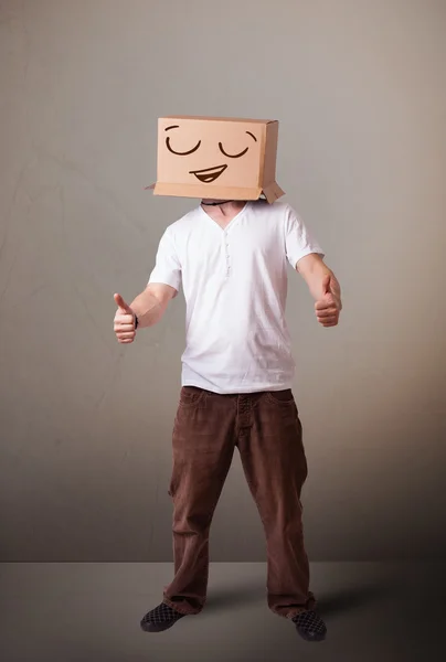 Young man gesturing with a cardboard box on his head with smiley — Stock Photo, Image