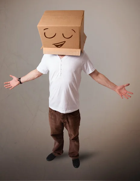 Joven haciendo un gesto con una caja de cartón en la cabeza con sonriente —  Fotos de Stock