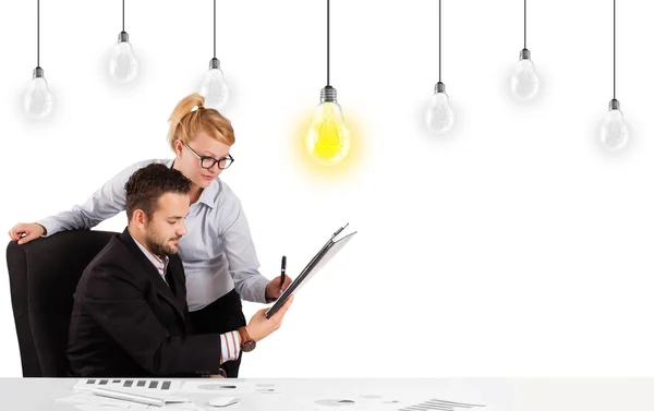 Hombre y mujer de negocios sentados a la mesa con bombillas de idea — Foto de Stock