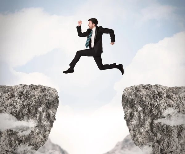 Hombre de negocios divertido saltando sobre rocas con brecha — Foto de Stock