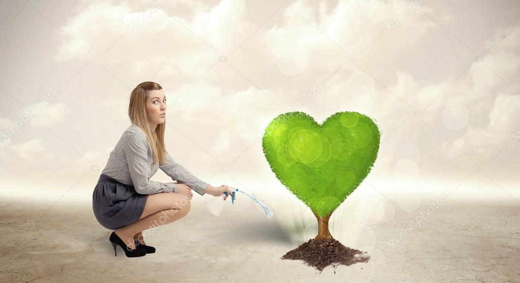 Business woman watering heart shaped green tree