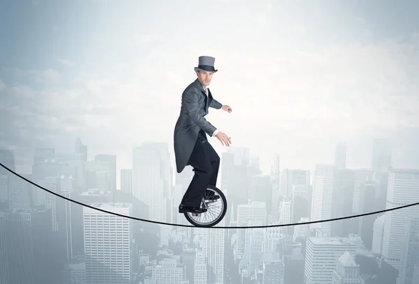 Brave guy riding a monocycle on a rope above cityscape — Stock Photo, Image