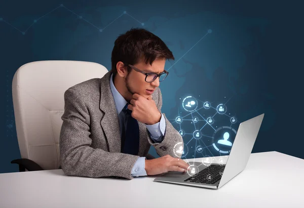 Jovem sentado na mesa e digitando no laptop com rede social — Fotografia de Stock