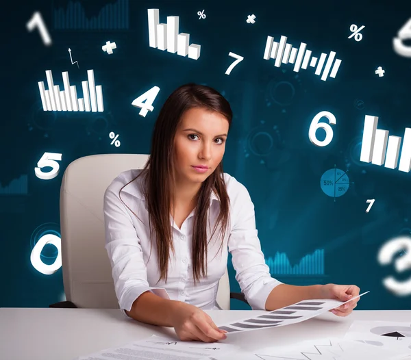 Giovane imprenditrice seduta alla scrivania con diagrammi e statistiche — Foto Stock