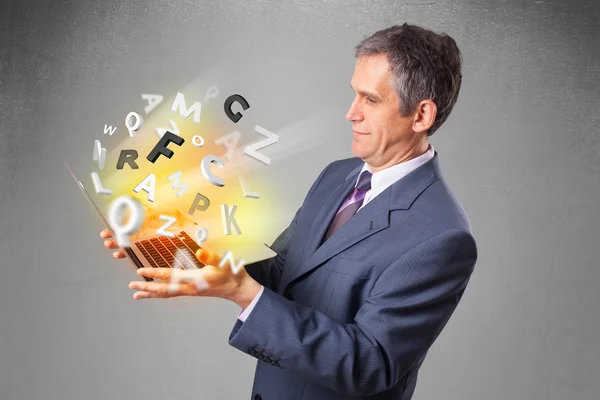 Middle aged businessman holding laptop with colorful letters — Stock Photo, Image