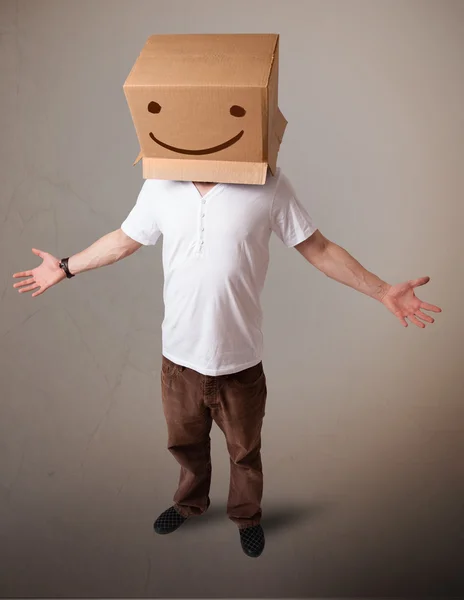 Young man gesturing with a cardboard box on his head with smiley — Stock Photo, Image