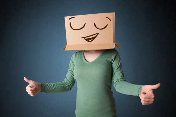 Jovem gesticulando com uma caixa de papelão na cabeça com smil — Fotografia de Stock