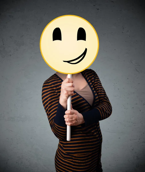 Young woman holding a smiley face emoticon — Stock Photo, Image