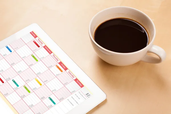 Tablet pc showing calendar on screen with a cup of coffee on a d — Stock Photo, Image