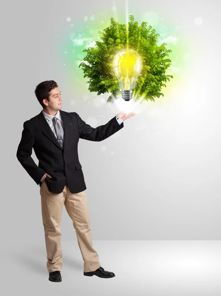 Νεαρός άνδρας παρουσιάζει λάμπα ιδέα με πράσινο δέντρο — Φωτογραφία Αρχείου