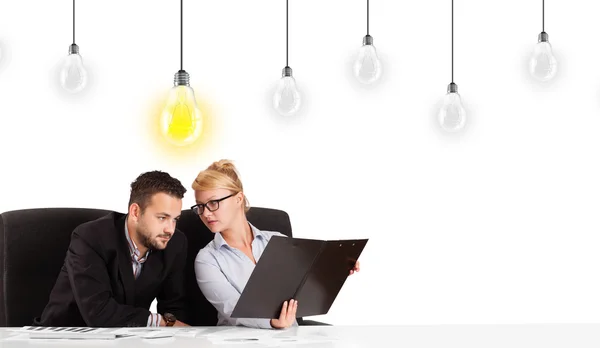 Business man och kvinna sitter vid bord med idé-lampor — Stockfoto