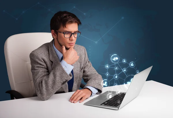 Jovem sentado na mesa e digitando no laptop com rede social — Fotografia de Stock