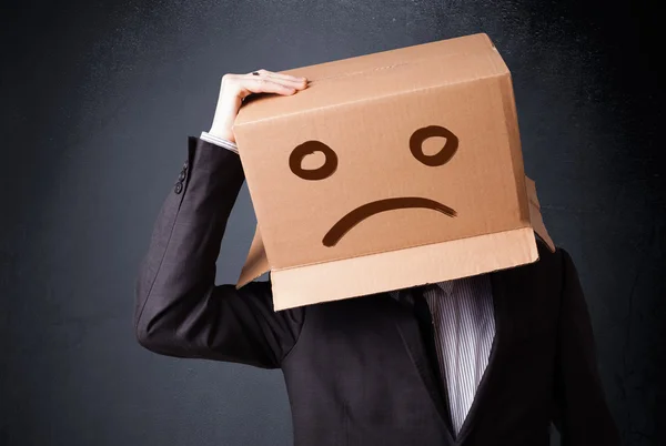 Empresário gesticulando com caixa de papelão na cabeça com fa triste — Fotografia de Stock