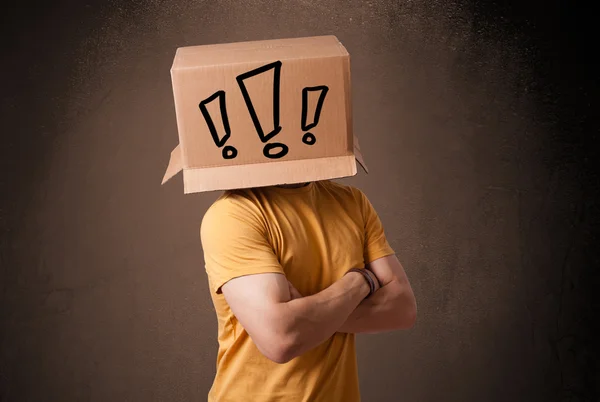 Young man gesturing with a cardboard box on his head with exclam — Stock Photo, Image