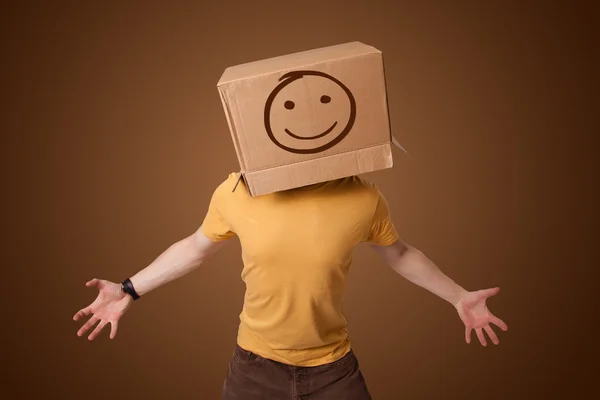 Ung man gestikulerande med en kartong på hans huvud med smiley — Stockfoto