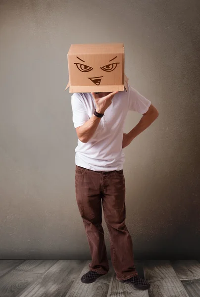 Young man gesturing with a cardboard box on his head with evil f — Stock Photo, Image