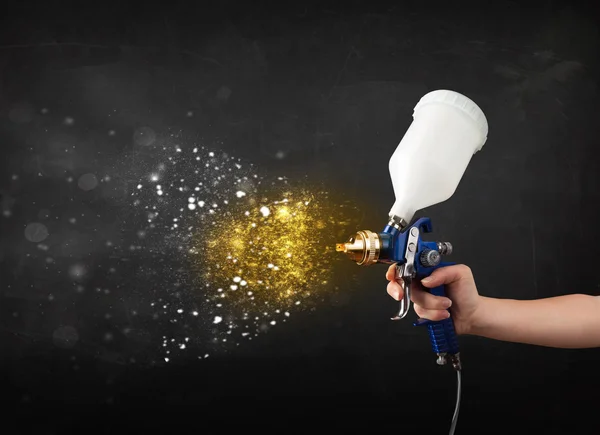 Worker with airbrush painting with glowing golden paint — Stock Photo, Image