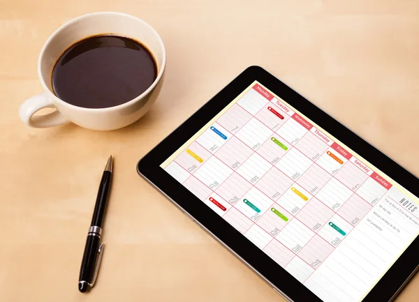 Tablet PC que muestra el calendario en la pantalla con una taza de café en una d —  Fotos de Stock