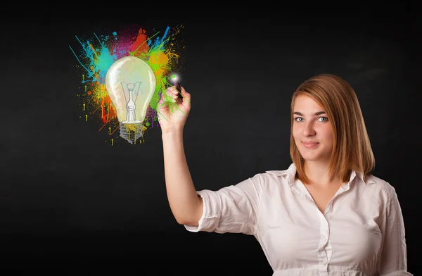 Young lady drawing a colorful light bulb with colorful splashes — Stock Photo, Image