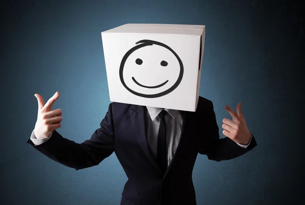 Empresario haciendo gestos con una caja de cartón en la cabeza con un sonrisas — Foto de Stock