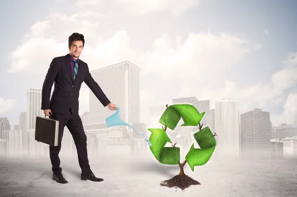 Business man watering green recycle sign tree on city background — Stock Photo, Image