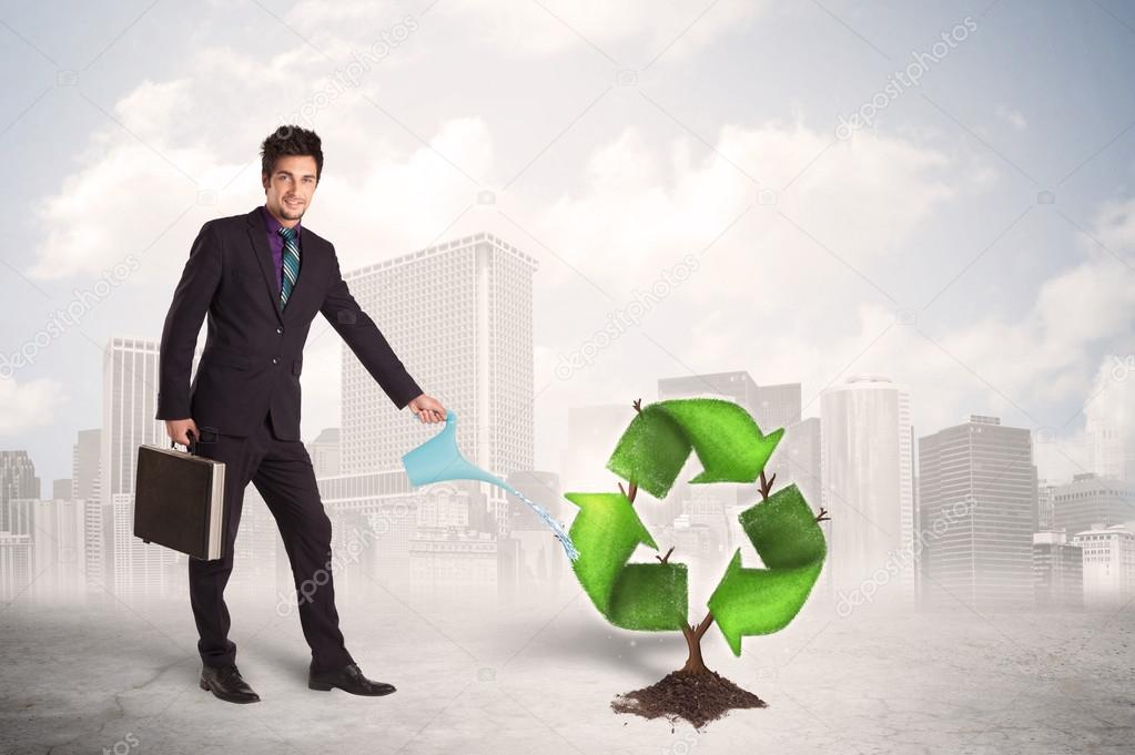 Business man watering green recycle sign tree on city background