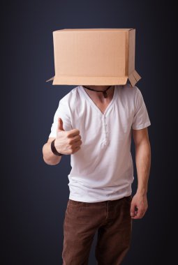 Kafasında karton bir kutuyla el kol hareketi yapan genç bir adam.