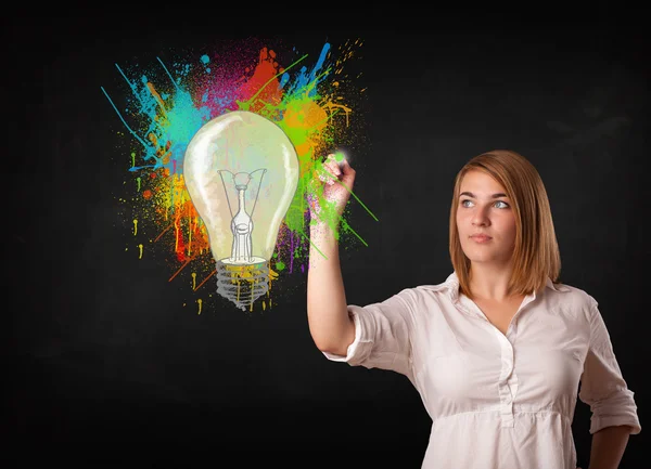 Young lady drawing a colorful light bulb with colorful splashes — Stock Photo, Image