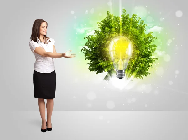 Молодая девушка представляет идею лампочки с зеленым деревом — стоковое фото