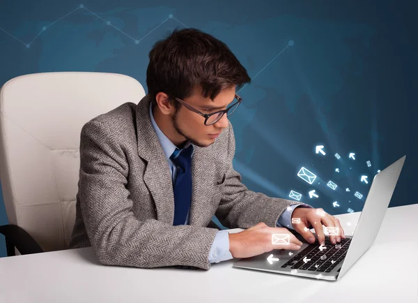 Mladý muž sedí na dest a psaní na notebooku s ikona zprávy — Stock fotografie