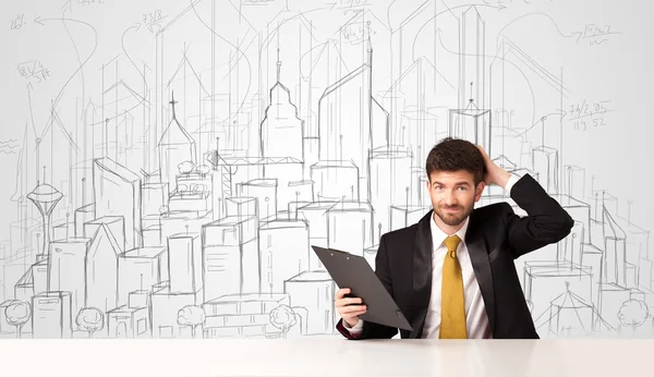 Businessman sitting at the white table with hand drawn buildings — Stock Photo, Image