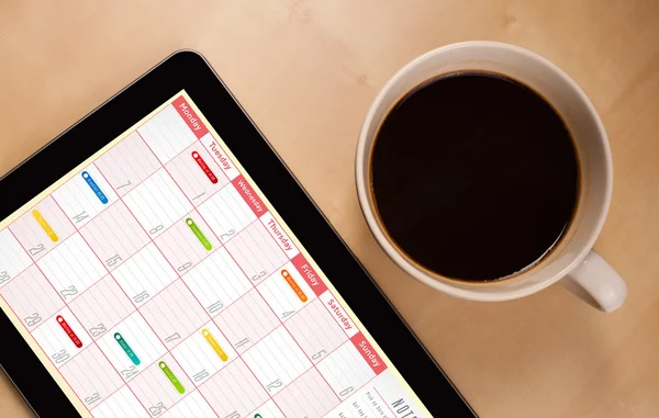 Tablet pc che mostra il calendario sullo schermo con una tazza di caffè su un d — Foto Stock