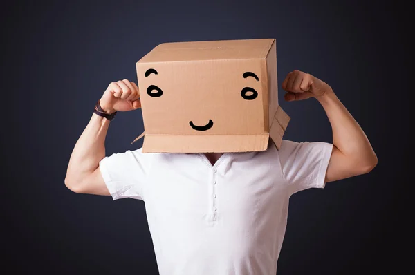 Jeune homme gesticulant avec une boîte en carton sur la tête avec un sourire — Photo