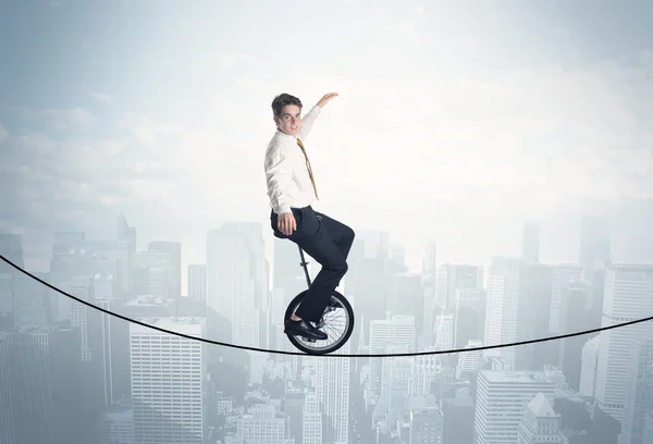 Brave guy riding a monocycle on a rope above cityscape — Stock Photo, Image