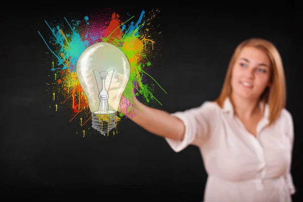 Young lady drawing a colorful light bulb with colorful splashes — Stock Photo, Image